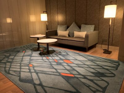 Esta imagem exibe uma sala de estar com pouca iluminação, um sofá e um tapete grande em primeiro plano.