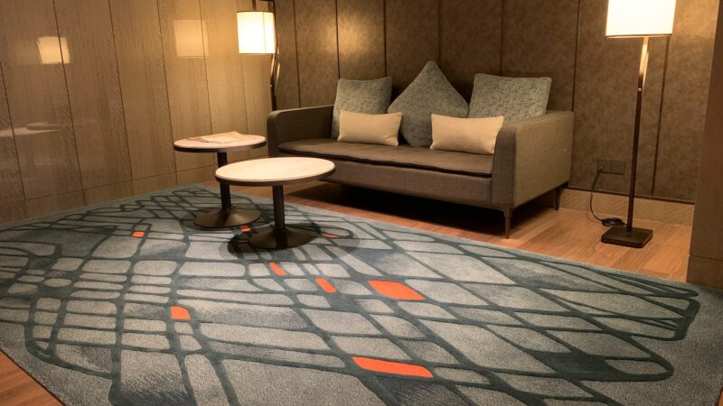 Esta imagem exibe uma sala de estar com pouca iluminação, um sofá e um tapete grande em primeiro plano.